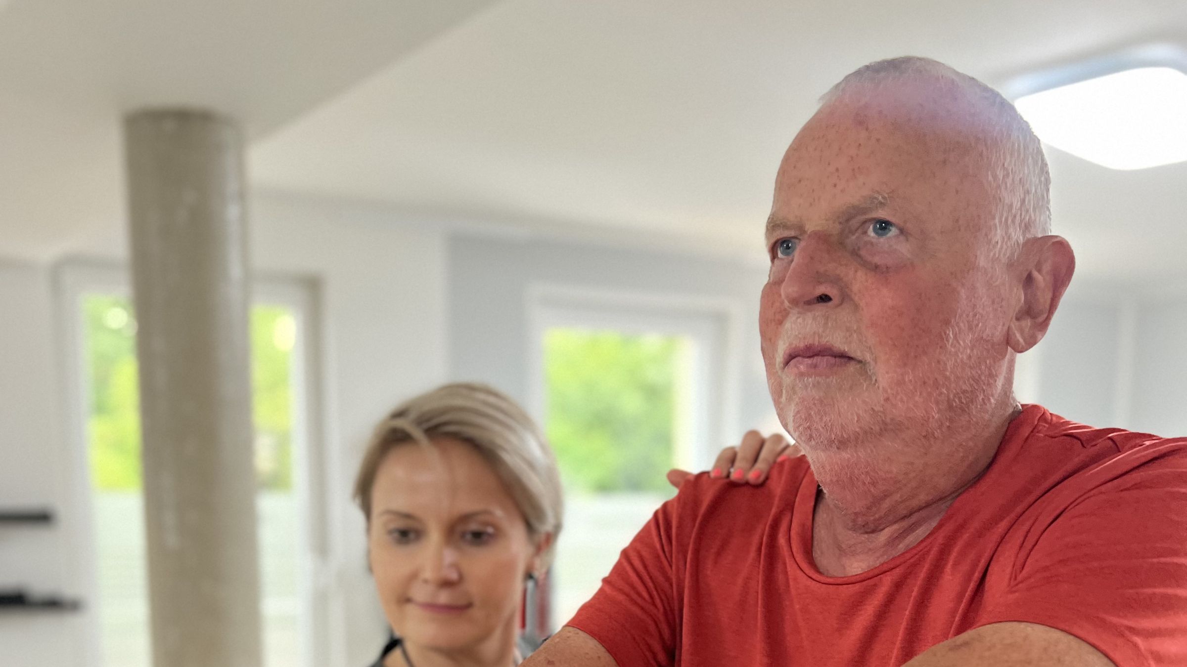 Patient trainiert am Seilzug, die Therapeutin im Praxisshirt steht hinter ihm