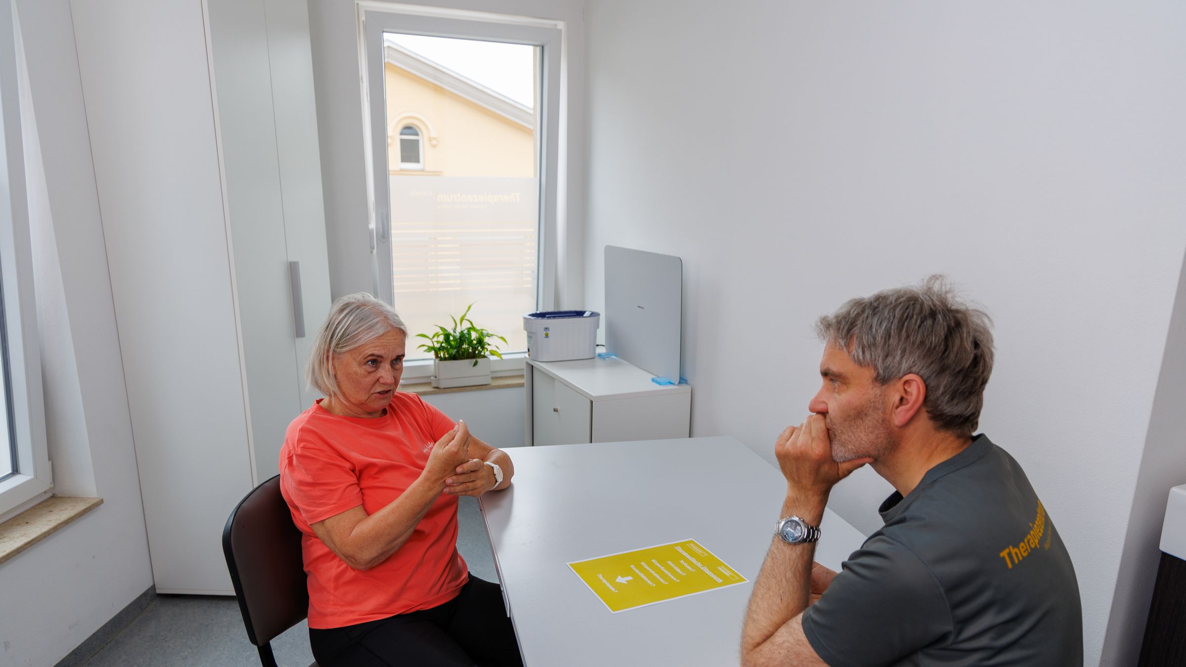 Therapeut und Patientin im Gespräch am Tisch, vor ihnen das gelbe Blatt