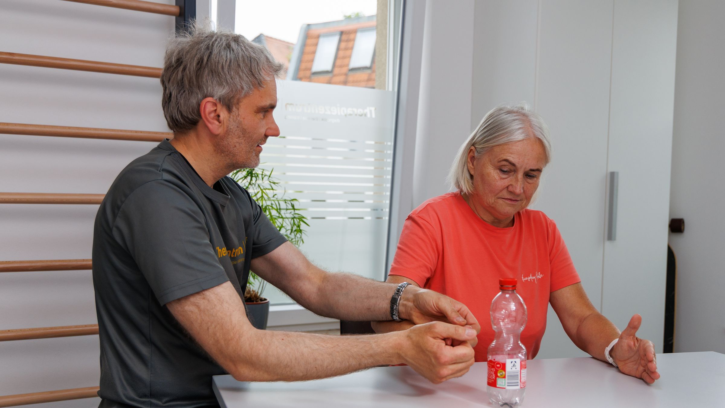 Therapeut untersucht die Hand einer Patientin am Tisch