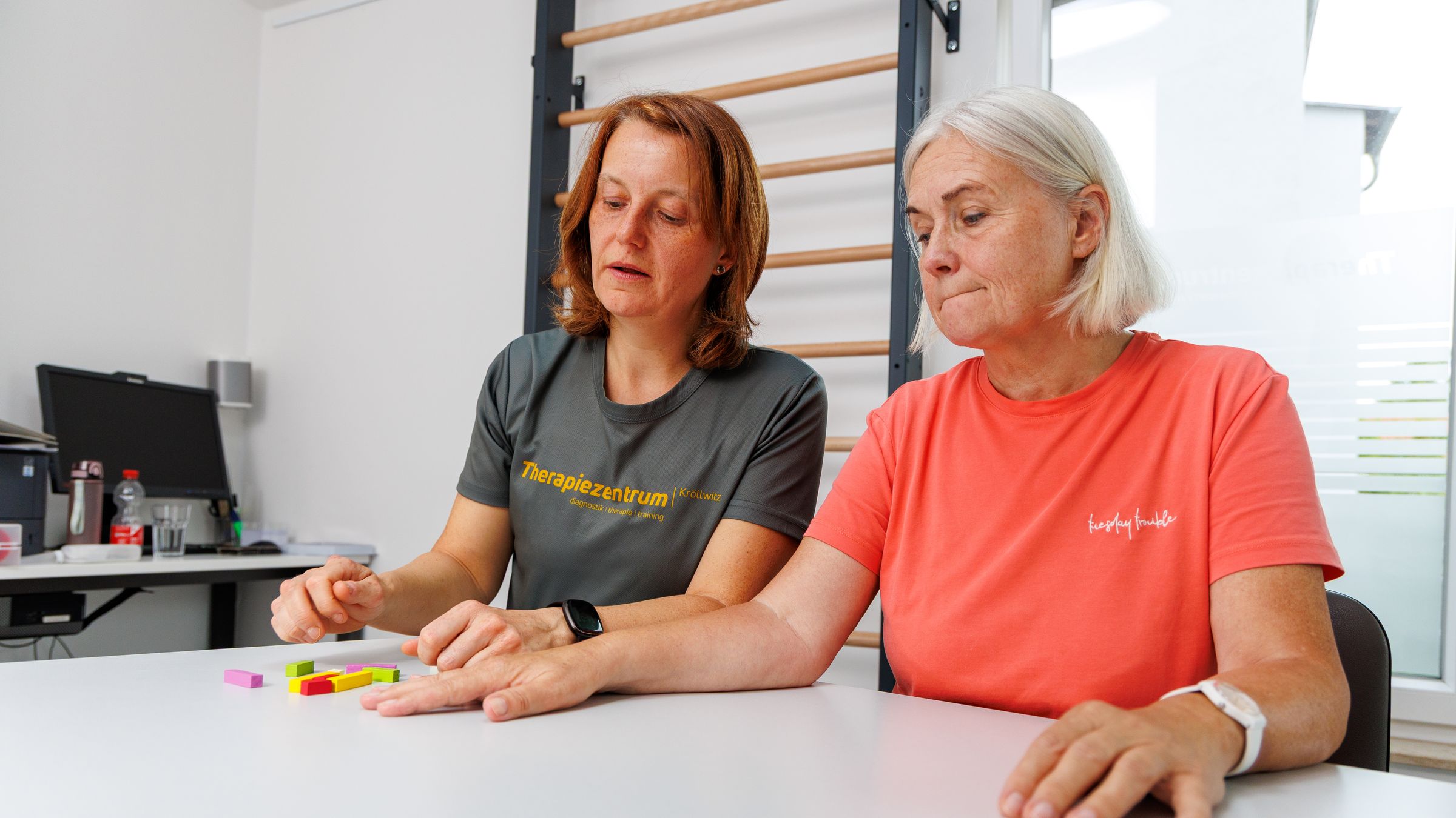 Ergotherapeutin und Patientin am Therapietisch mit farbigen Holzklötzen
