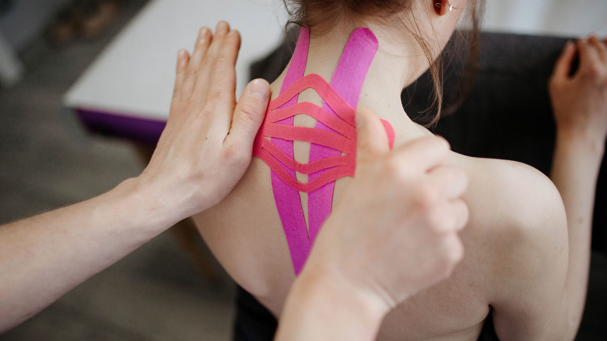 Kinesiotape auf Nacken und Schulter, die Hände der Therapeutin streichen es an