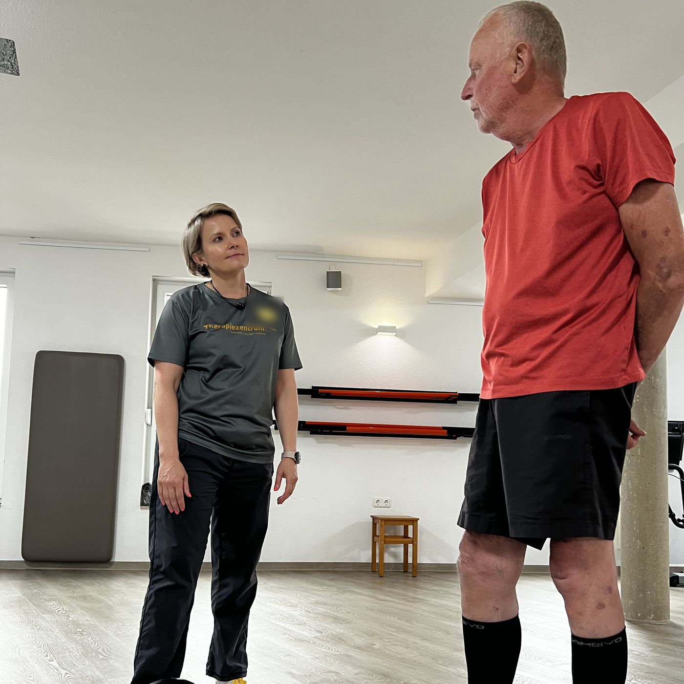Therapeutin und Patient stehen sich auf der Trainingsfläche gegenüber und sprechen miteinander