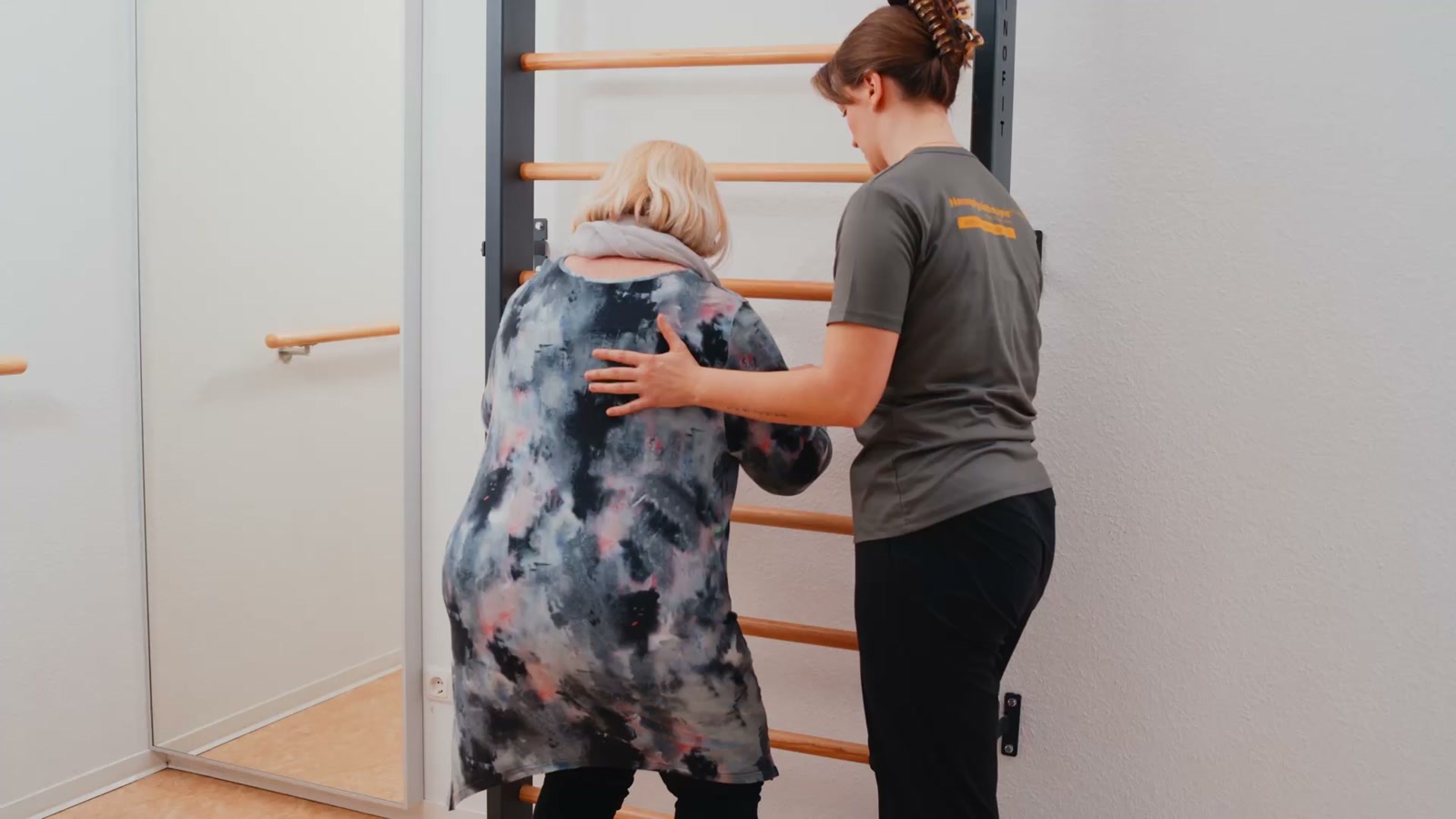 Therapeutin begleitet eine Patientin beim Gehen an der Sprossenwand